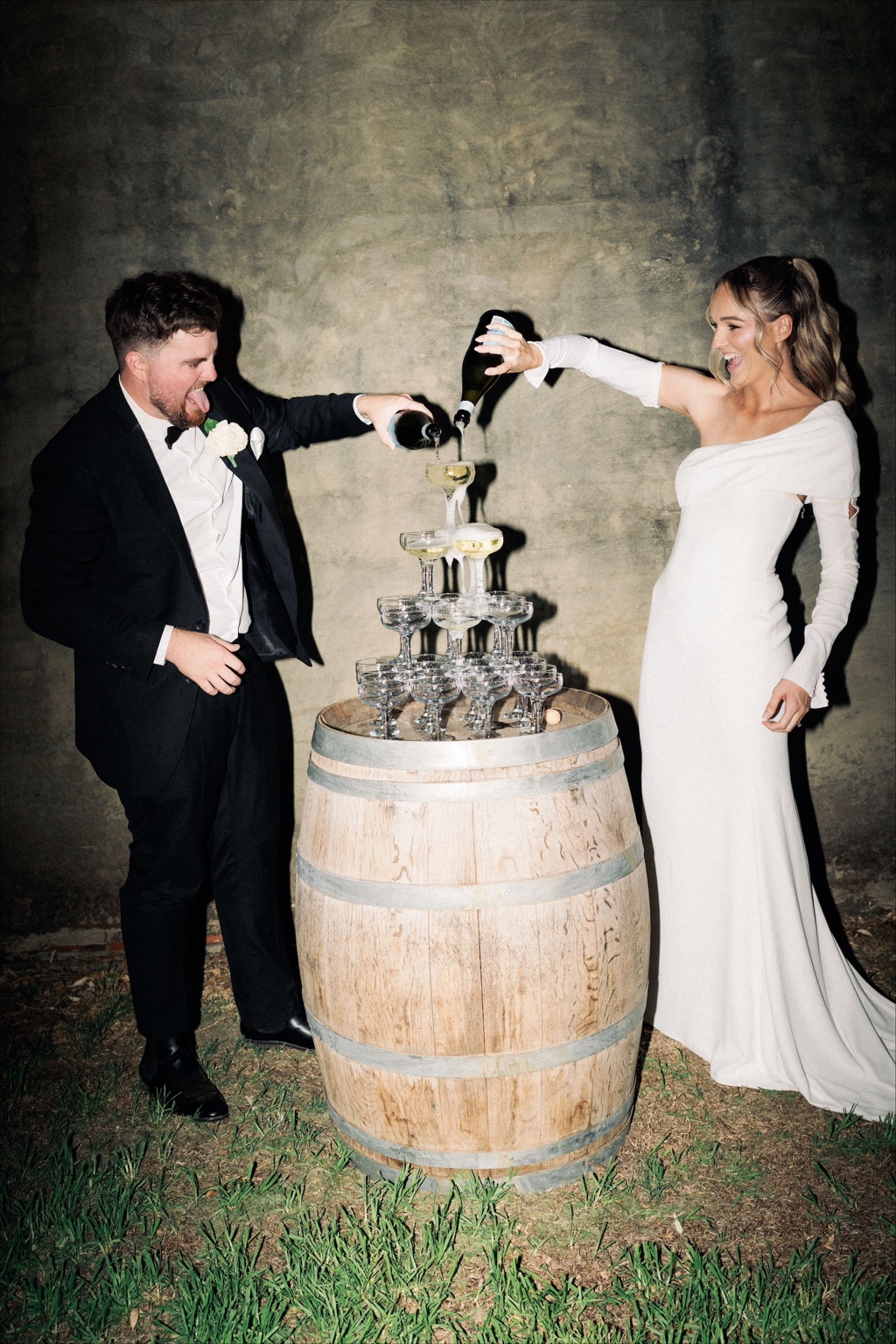 A couple pouring sparkling wine into a tower of coupe glasses